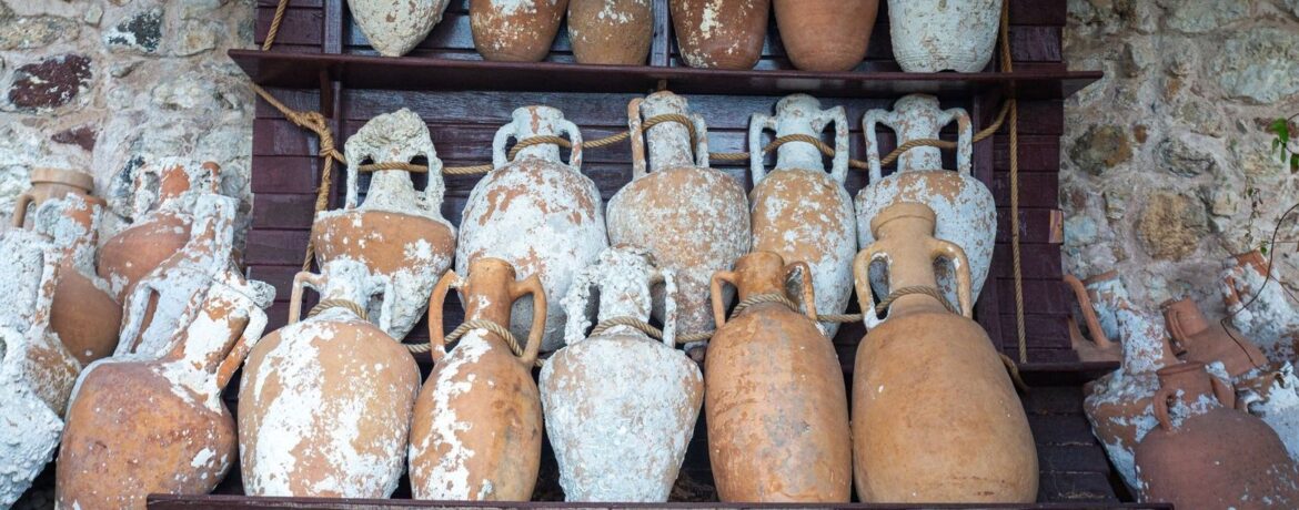 Weathered terracotta amphorae displayed on wooden racks against a stone wall